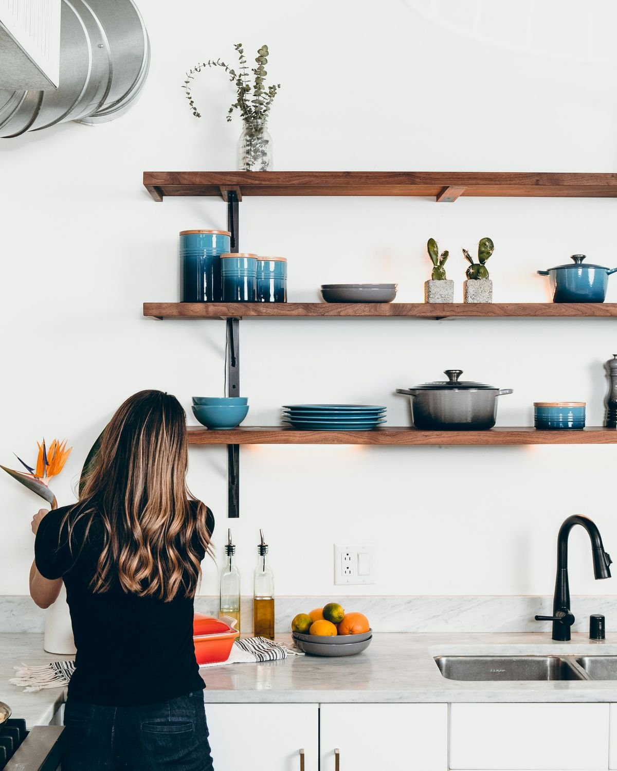 Woman organizing open kitchen shelves with cookware, dishes and kitchen essentials for 5 best kitchen gadgets that make everyday cooking easier
